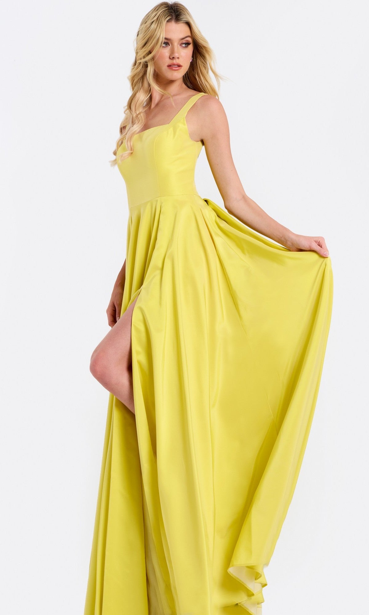 A woman poses in the Jovani 47496, a sleeveless long prom dress with an A-line flowy skirt and thigh-high slit, holding the side of her gown.